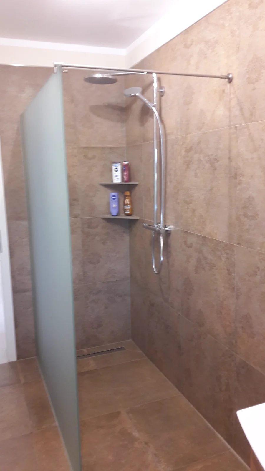 Dusche mit mattierter Glasseitenwand Dusche mit mattierter Glasseitenwand, oberer Stabilisierungsstange und braunen Wandfliesen.