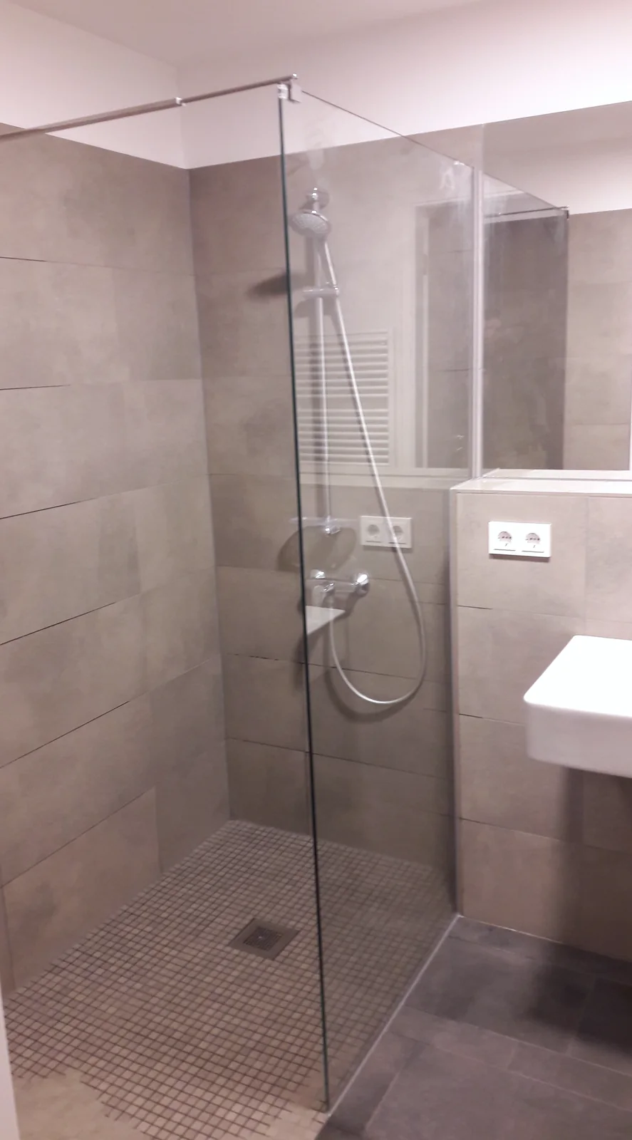 Schmale Dusche mit Glasabtrennung Schmale bodengleiche Dusche mit transparenter Glasabtrennung, Stabilisierungsstange und Mosaikboden.