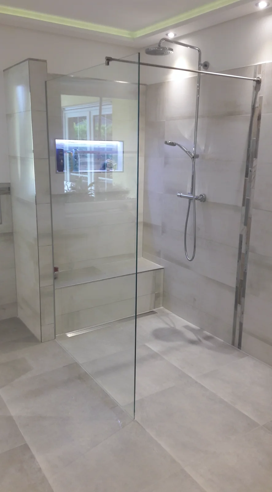 Walk-in-Dusche mit Glasabtrennung Bodengleiche Dusche mit rahmenloser Glasabtrennung, Stabilisierungsstange und gefliester Sitzbank.